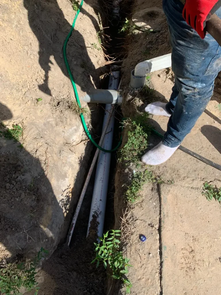 Excavated trench showing exposed PVC drain pipes and fittings before sealing with a clamping ring connection.
