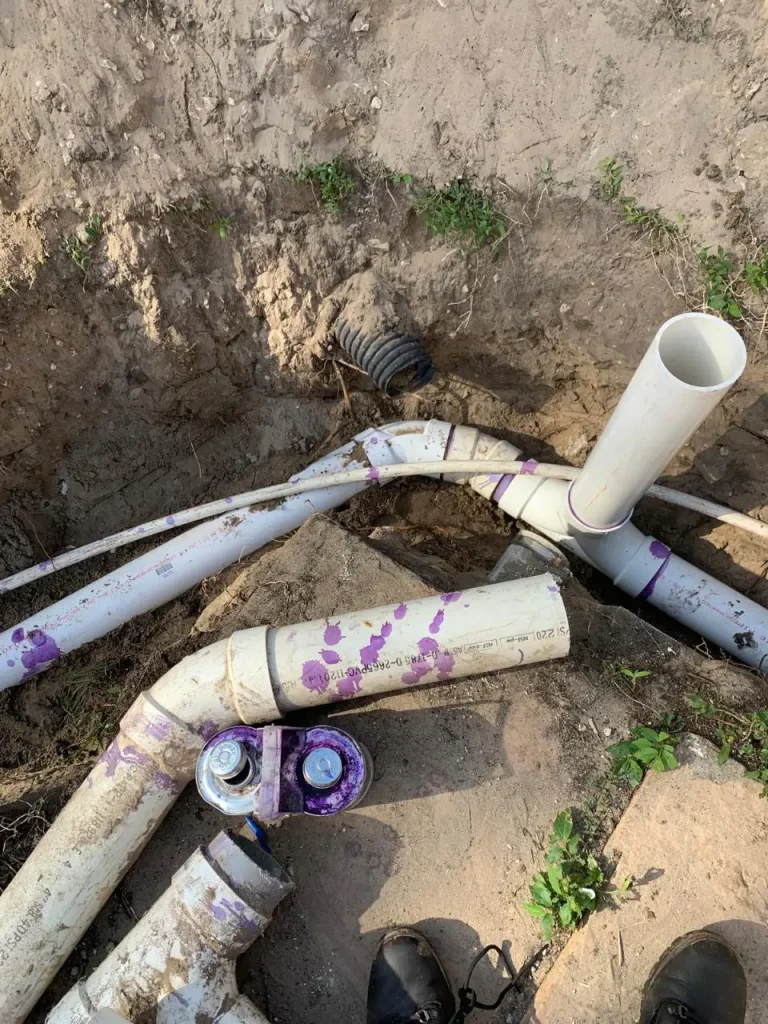 Close-up of underground PVC plumbing joint with visible clamping ring used to secure and seal drain connections.